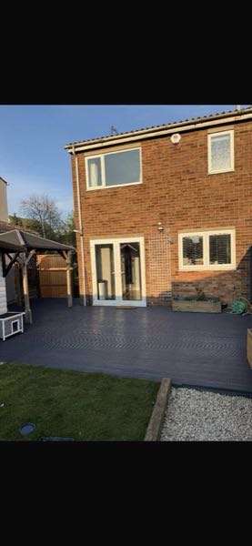 Grey composite decking laid across the back of a house, with a gravel border and corner pergola